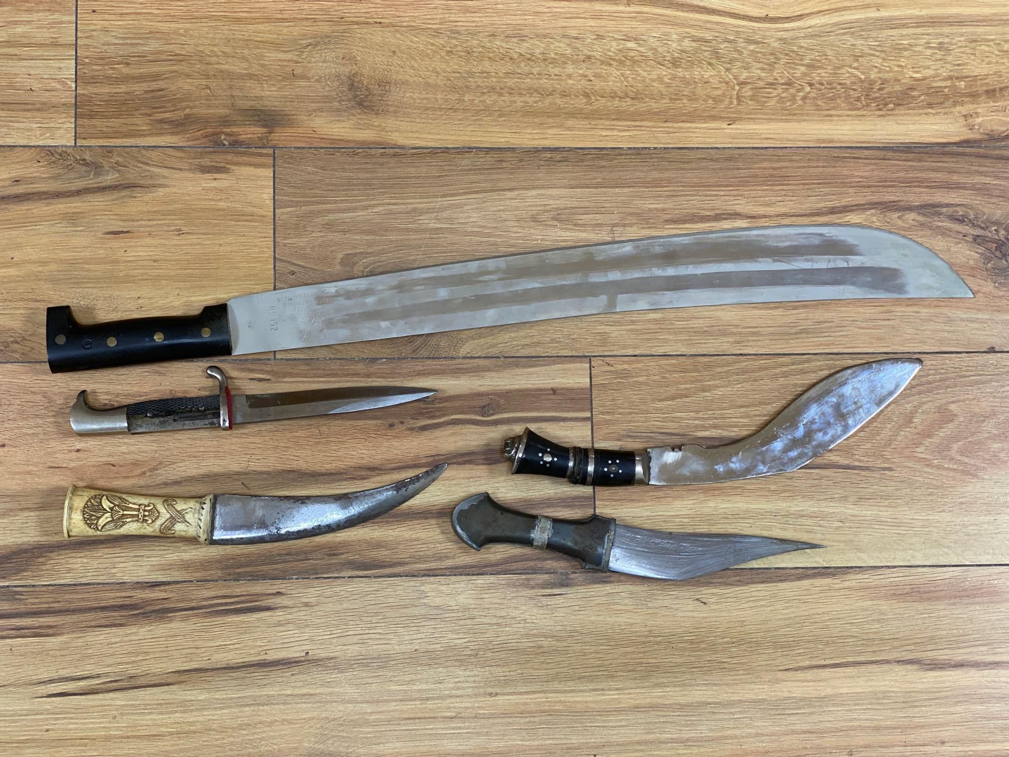 Five various weapons including a Kukri, a carved bone handled dagger with brass sun, moon and stars sheath and an El Salvador machete